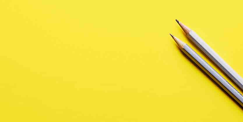 Two sharpened pencils with white bodies placed parallel to each other on a bright yellow background, positioned on the right side of the image.